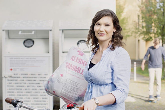 Kleidersammlung des DRK und Altkleidercontainer: junge Frau mit Altkleidersack vor einem Container des DRK- 2014