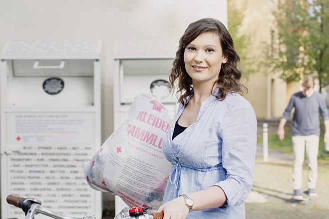 Kleidersammlung des DRK und Altkleidercontainer: junge Frau mit Altkleidersack vor einem Container des DRK- 2014