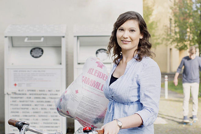 Kleidersammlung des DRK und Altkleidercontainer: junge Frau mit Altkleidersack vor einem Container des DRK- 2014