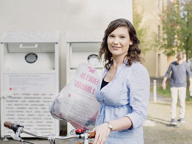 Kleidersammlung des DRK und Altkleidercontainer: junge Frau mit Altkleidersack vor einem Container des DRK- 2014